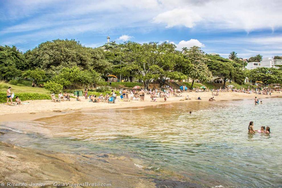 Imagem de turistas nas areias e crianças nas águas.